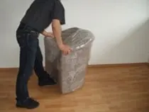Ein Möbelpacker umwickelt einen Polstersessel mit Verpackungsfolie